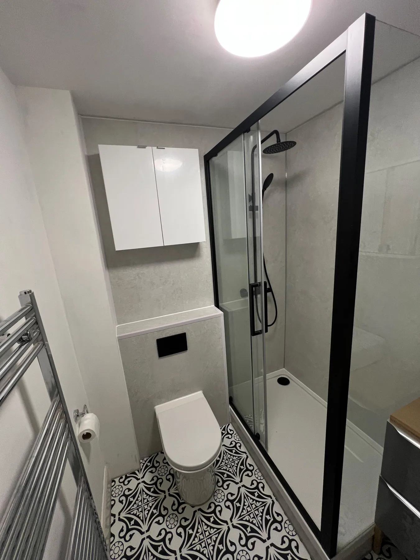 Compact shower room with black screen, toilet and patterned flooring