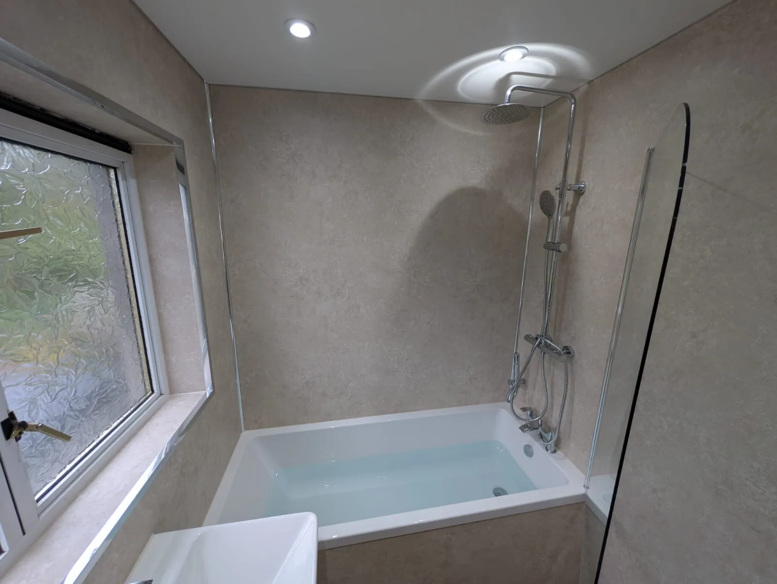 Fitted bath with clear glass screen and neutral wall panels
