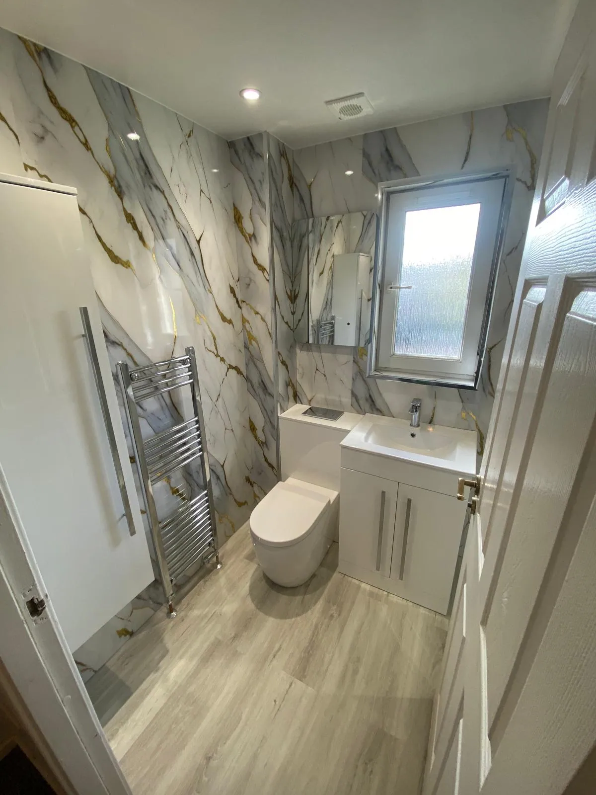 White vanity and toilet with gold-veined marble-effect wall panels