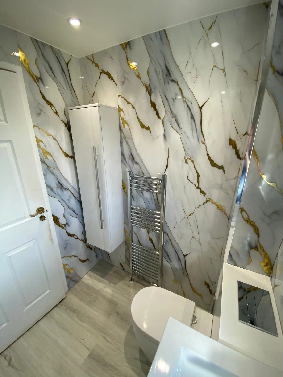 Tall white bathroom cupboard beside chrome towel rail